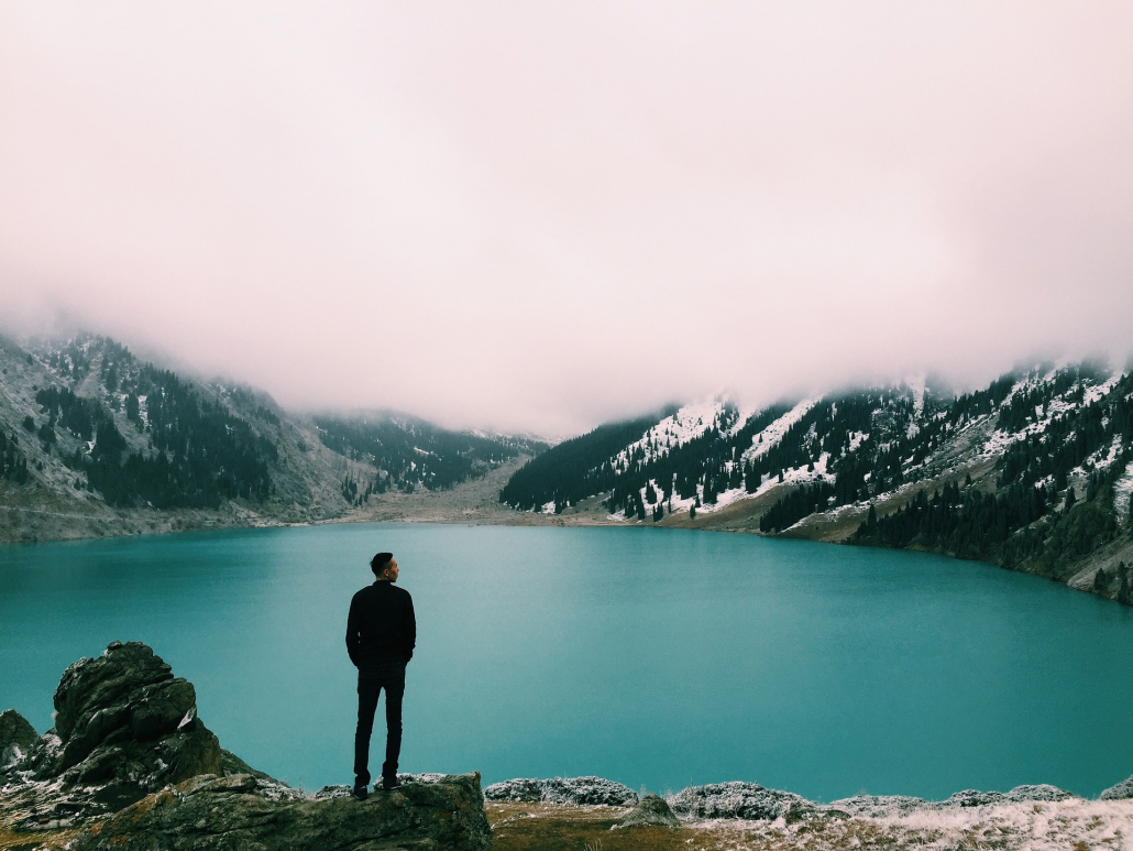 Ein Mann steht vor einem türkisenem Bergsee und schaut in die Landschaft.