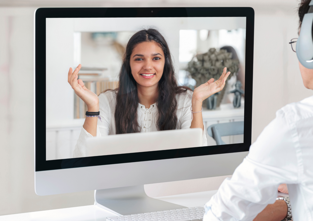 Ein Mann führt eine Videokonferenz mit einer Frau, welche zentral auf einem Bildschirm angezeigt wird. 